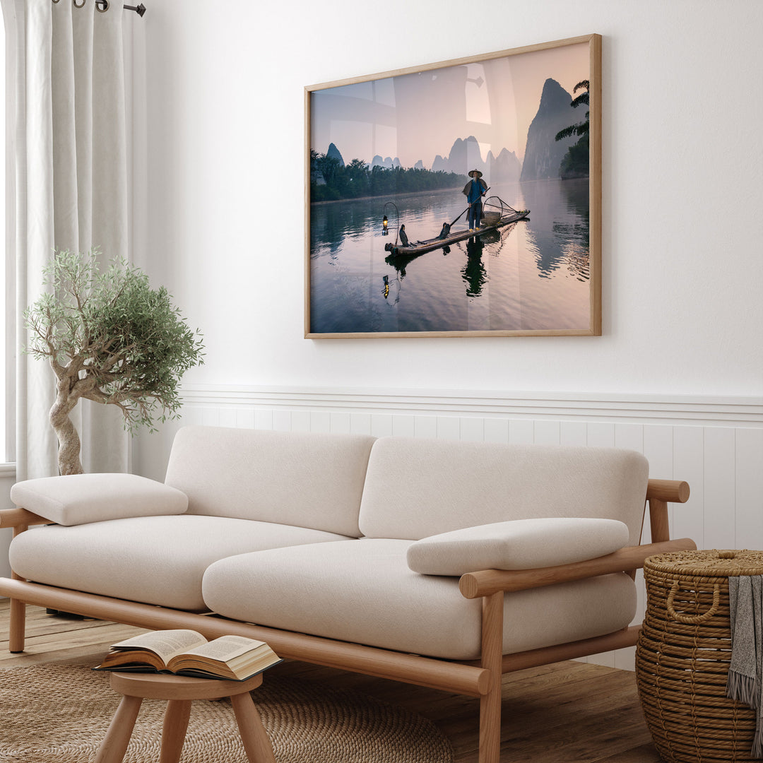 a serene living room with a large framed picture of a person on a boat on the wall, a white sofa, a wooden stool, and a potted plant.