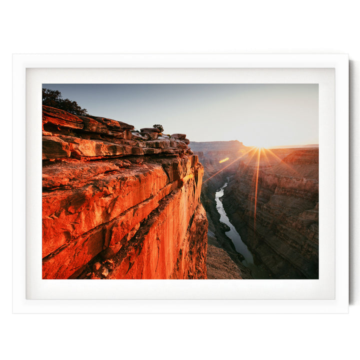 A breathtaking view of a canyon at sunset, with the sun's rays shining down on the rugged, red rock formations and a winding river below.