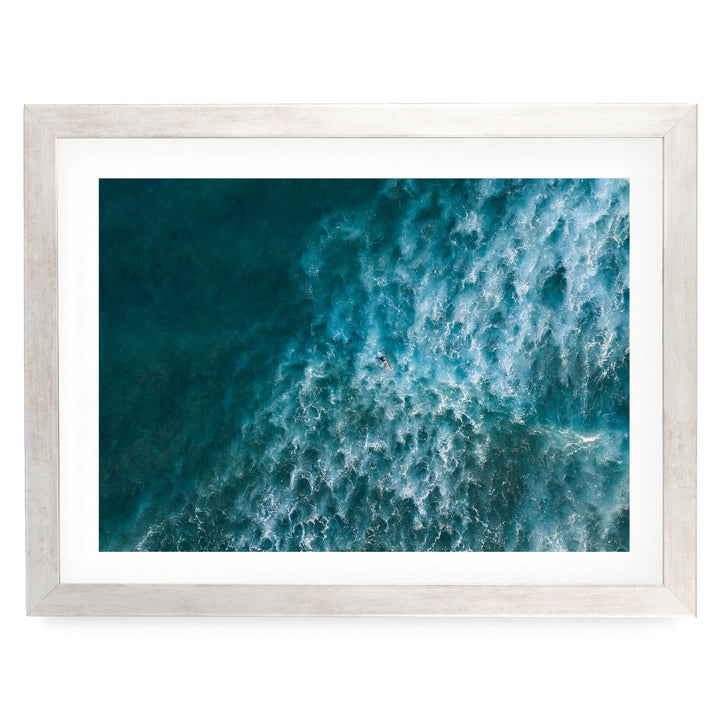 The image is a framed aerial view of a vast, turquoise ocean with waves crashing against the shore.