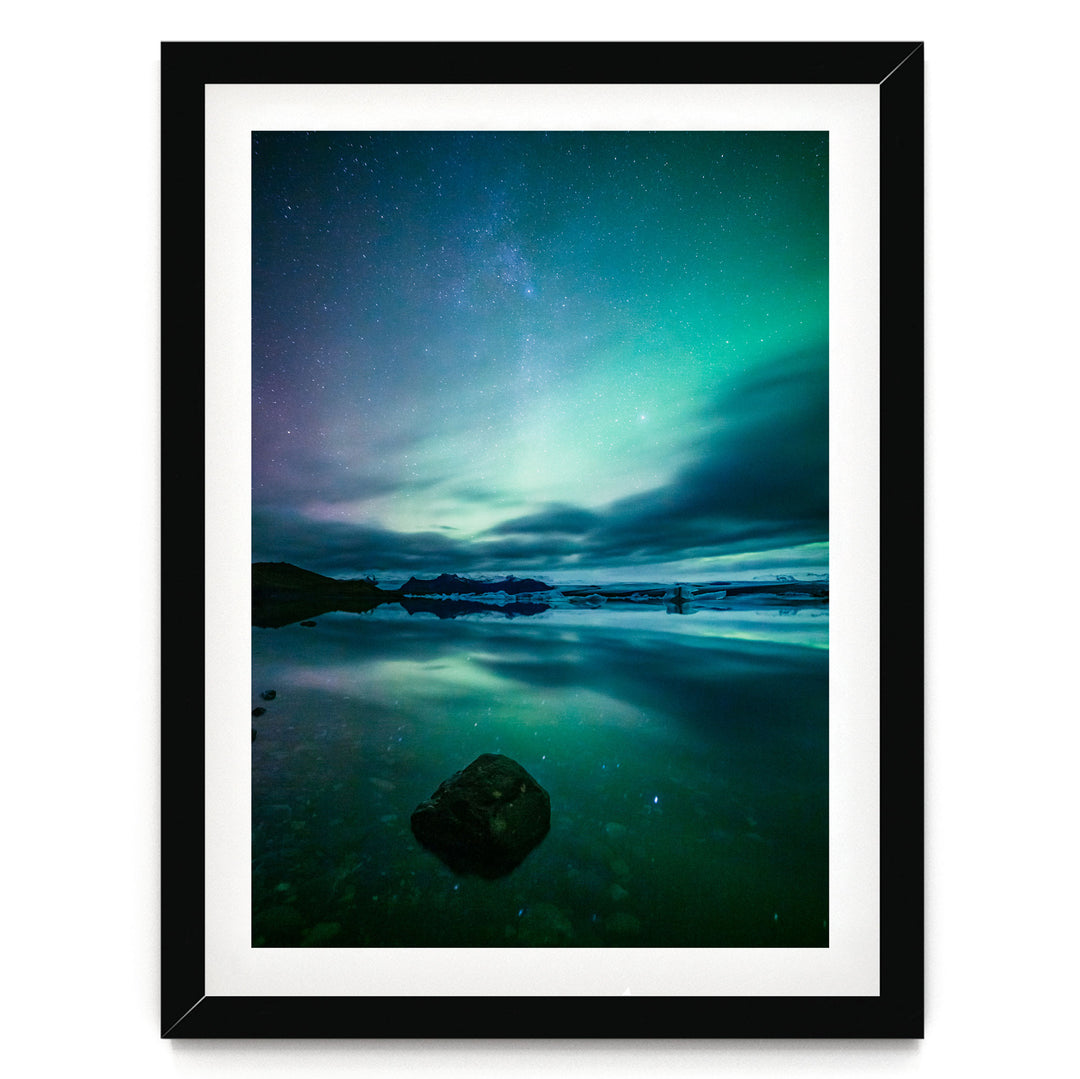 a serene night scene with a calm body of water reflecting the vibrant colors of the night sky, including shades of blue, green, and purple.