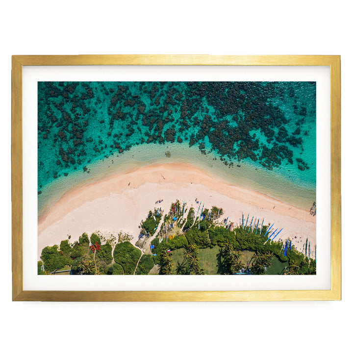 The image is an aerial view of a tropical beach with a sandy shore, lush vegetation, and a clear turquoise ocean.