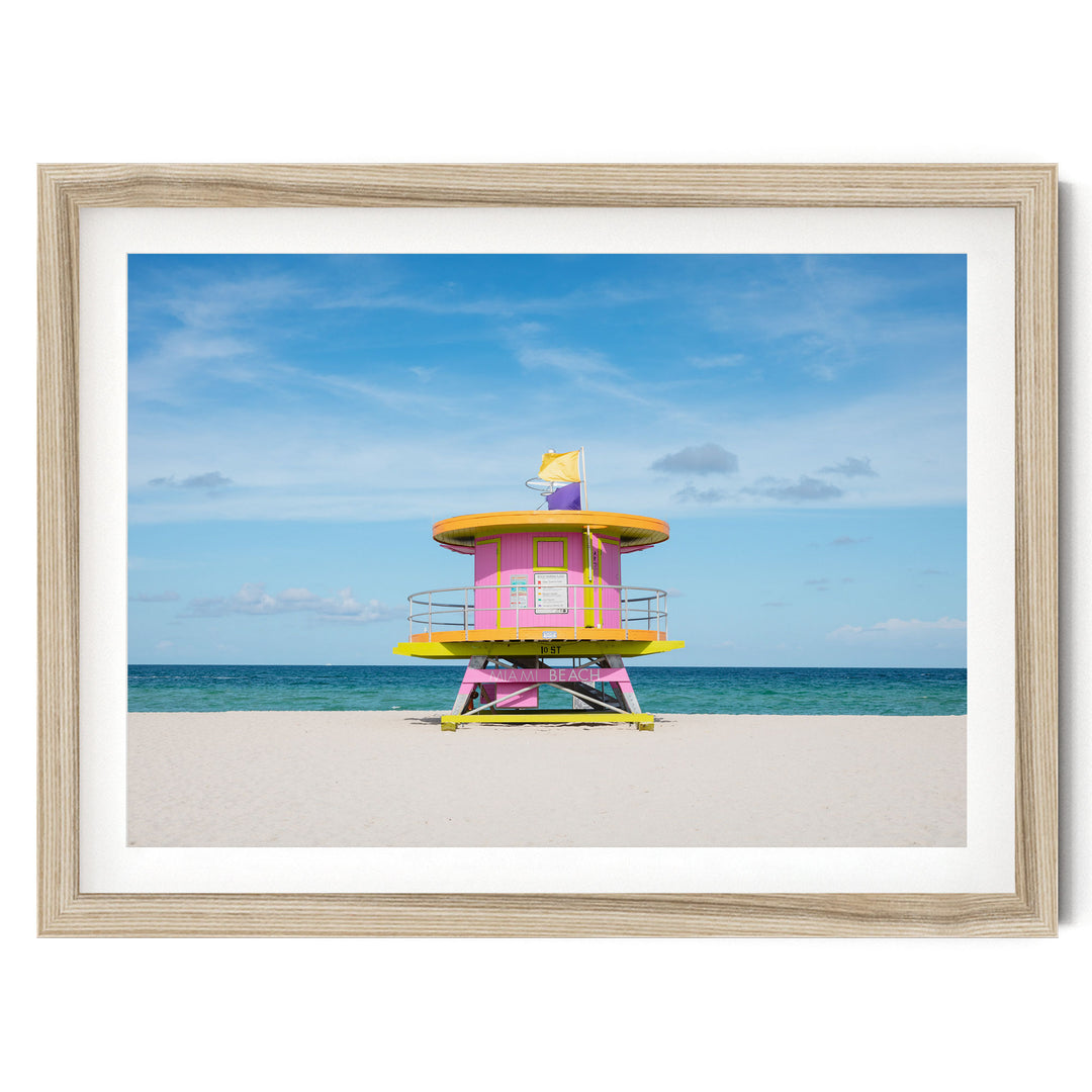 A lifeguard tower painted in vibrant pink and yellow stands on a sandy beach, overlooking the ocean.