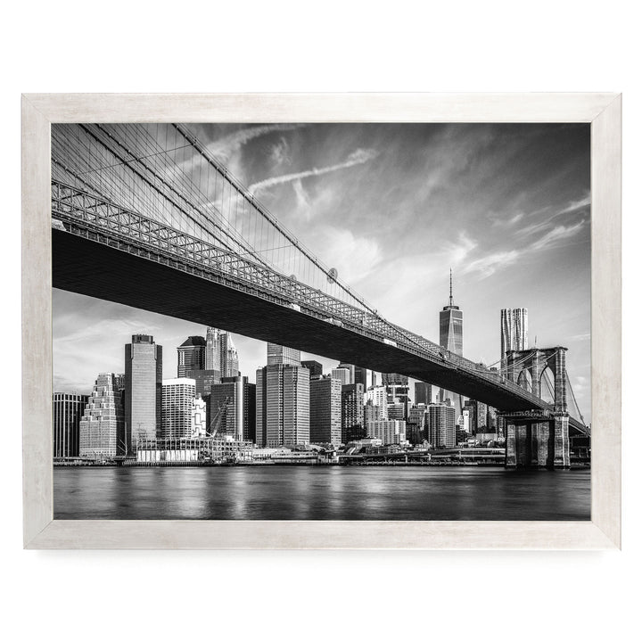 A black and white photograph of the Brooklyn Bridge spanning the East River, with the New York City skyline visible in the background.