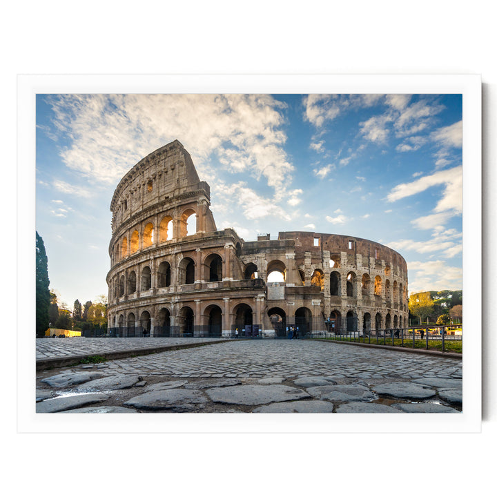 the Colosseum, an ancient amphitheater in Rome, Italy, with its distinctive curved walls and arches. The Colosseum is set against a backdrop of a blue sky with white clouds, creating a striking contrast. The photograph is taken from a low angle, emphasizing the grandeur and imposing nature of the structure.