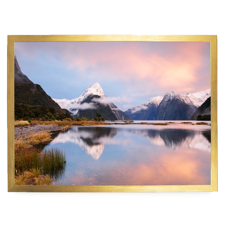 a serene landscape with a calm lake reflecting the surrounding mountains and sky. The mountains are covered in snow, and the sky is a beautiful gradient of pink and blue, creating a picturesque scene.