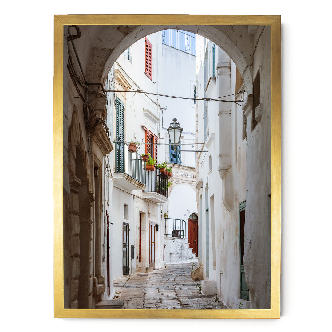 a narrow, cobblestone street lined with white buildings featuring colorful shutters and balconies.