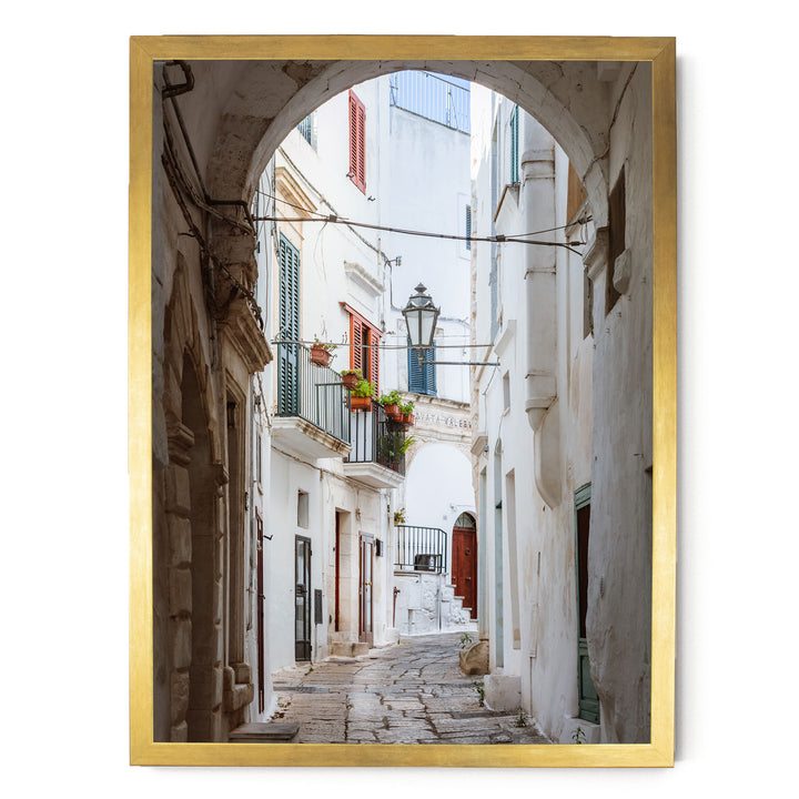a narrow, cobblestone street lined with white buildings featuring colorful shutters and balconies.