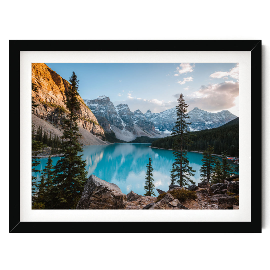 A framed photograph depicting a serene mountain landscape with a deep blue lake surrounded by snow-capped peaks and pine trees.