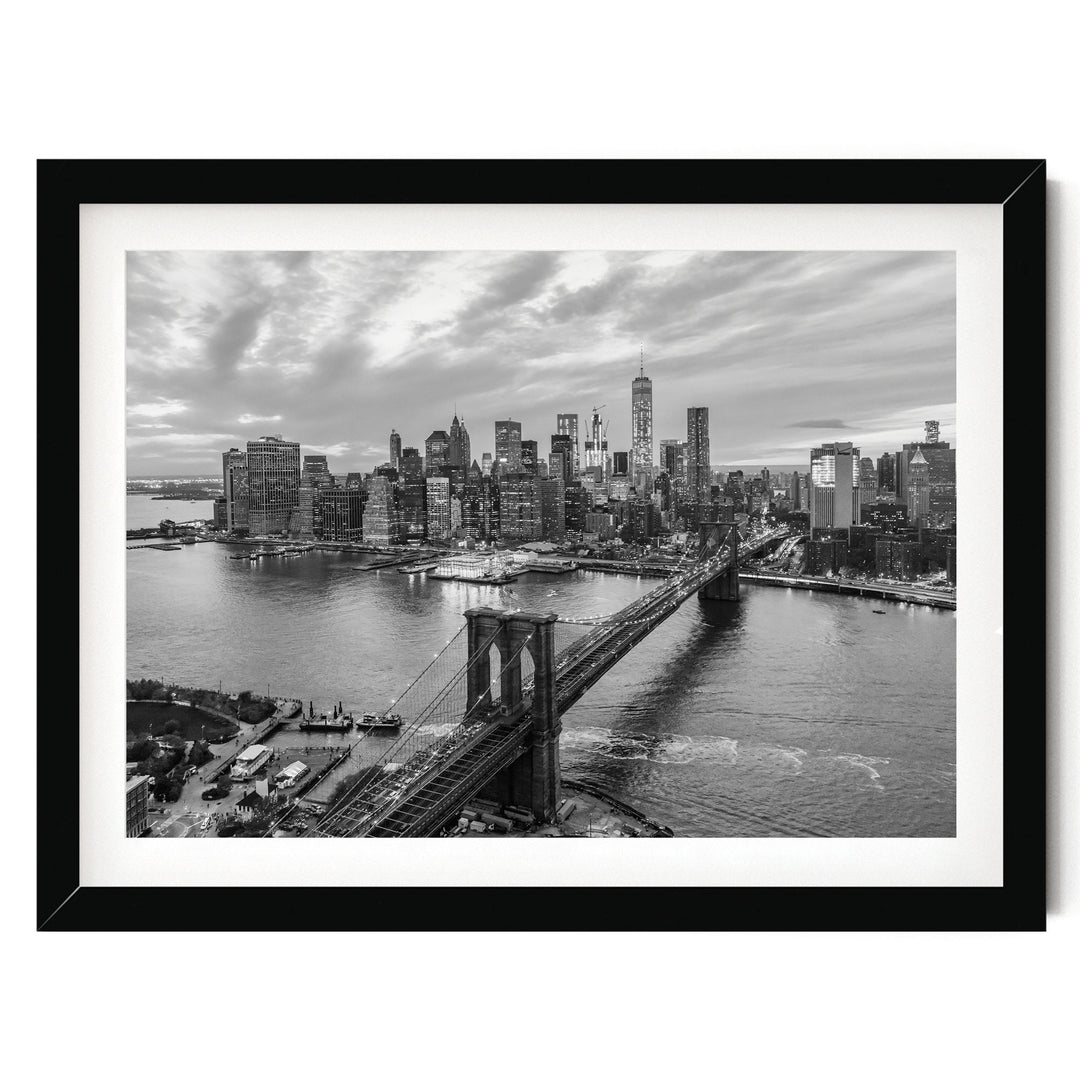 A black and white photograph of the New York City skyline, featuring the Brooklyn Bridge and the surrounding cityscape.