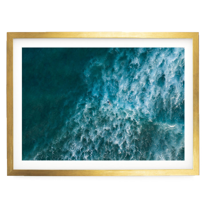 The image is a framed aerial view of a large body of water, likely an ocean, with waves and a person visible in the water.