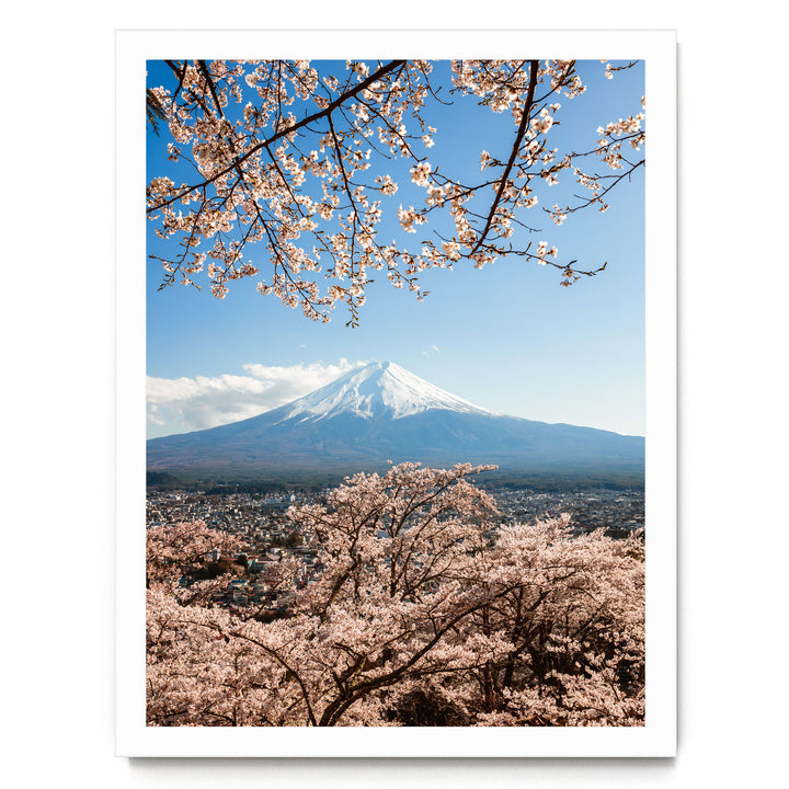 A breathtaking view of Mount Fuji, the iconic snow-capped peak of Japan, set against a clear blue sky with cherry blossoms in full bloom in the foreground.
