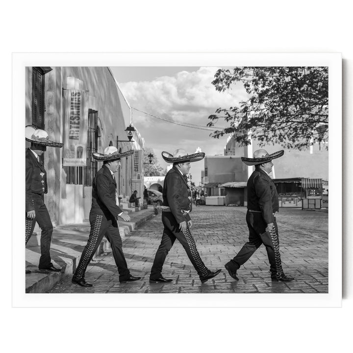 A group of men wearing sombreros and suits are walking down a street, with buildings and trees in the background.