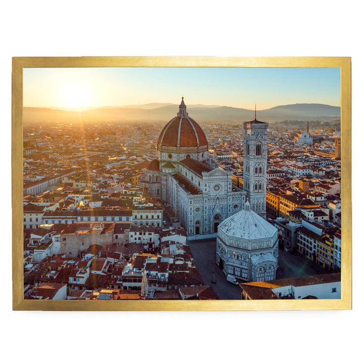 a cityscape with a large domed building, possibly a cathedral or church, surrounded by smaller buildings and structures. The sun is setting, casting a warm glow over the scene.