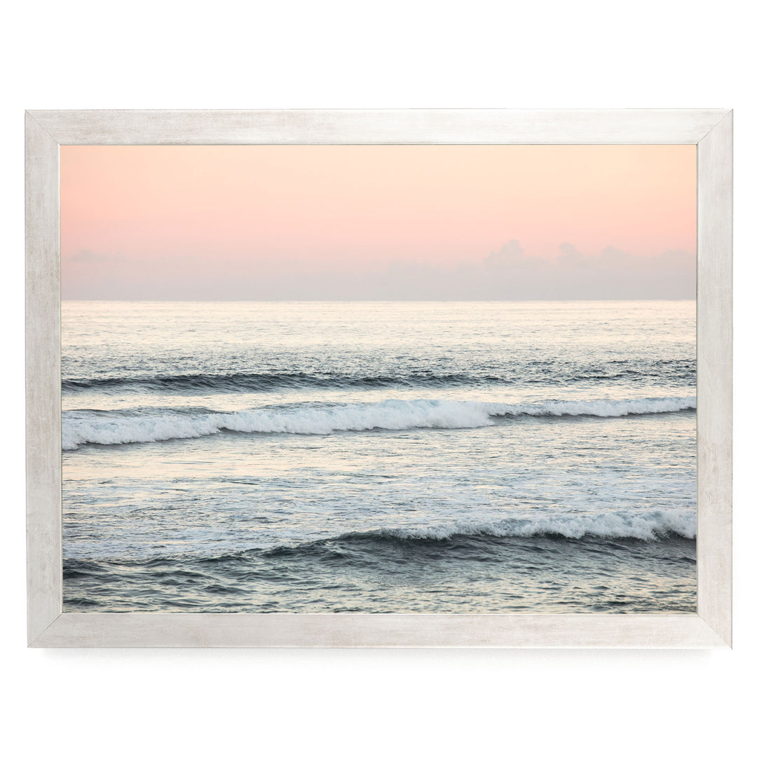 a serene ocean scene with waves gently lapping against the shore, set against a backdrop of a hazy pink sky.