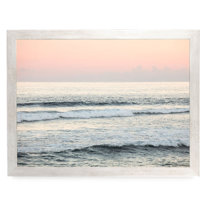 a serene ocean scene with waves gently lapping against the shore, set against a backdrop of a hazy pink sky.