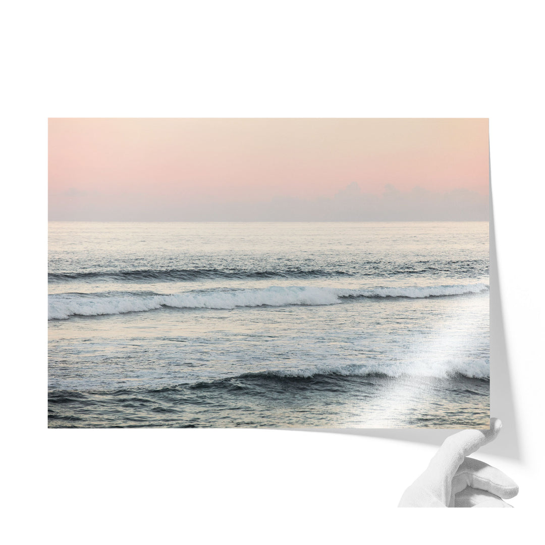 A hand is holding a piece of paper with a serene image of a sunset over the ocean, featuring waves crashing against the shore.