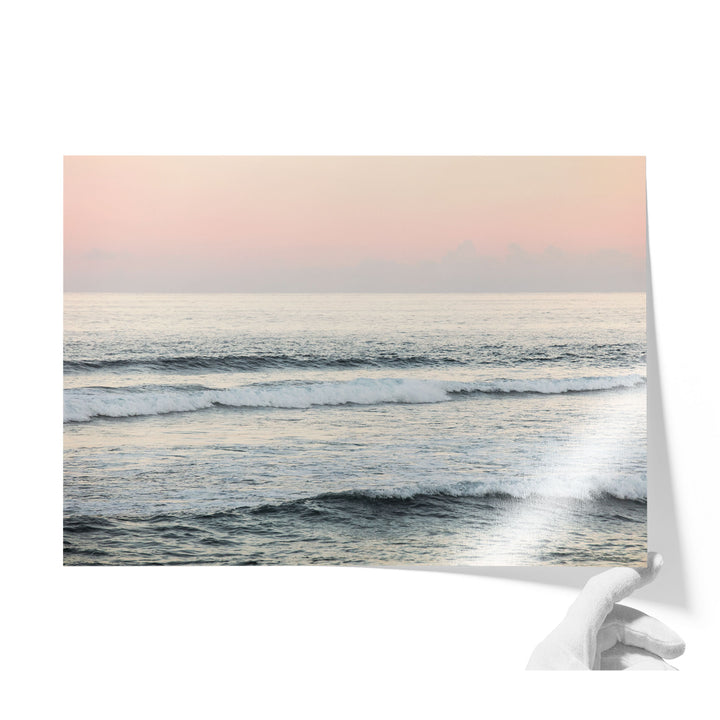 A hand is holding a piece of paper with a serene image of a sunset over the ocean, featuring waves crashing against the shore.