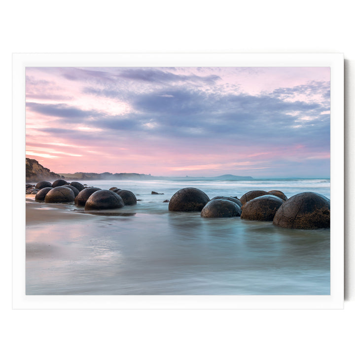 A serene beach scene with a collection of large, round boulders in the water, set against a vibrant sunset sky.