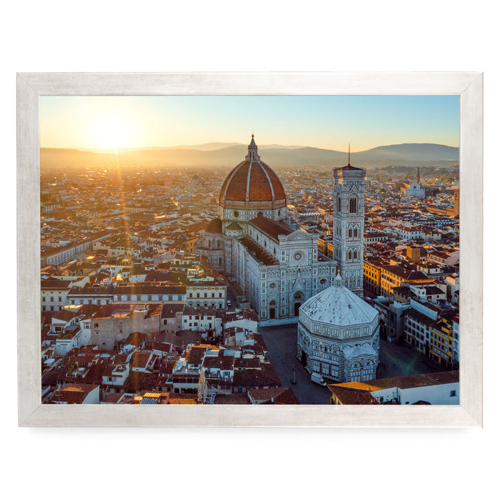 a cityscape with a large, domed cathedral in the center, surrounded by smaller buildings and structures. The sun is setting, casting a warm glow over the scene and creating a picturesque view of the city.
