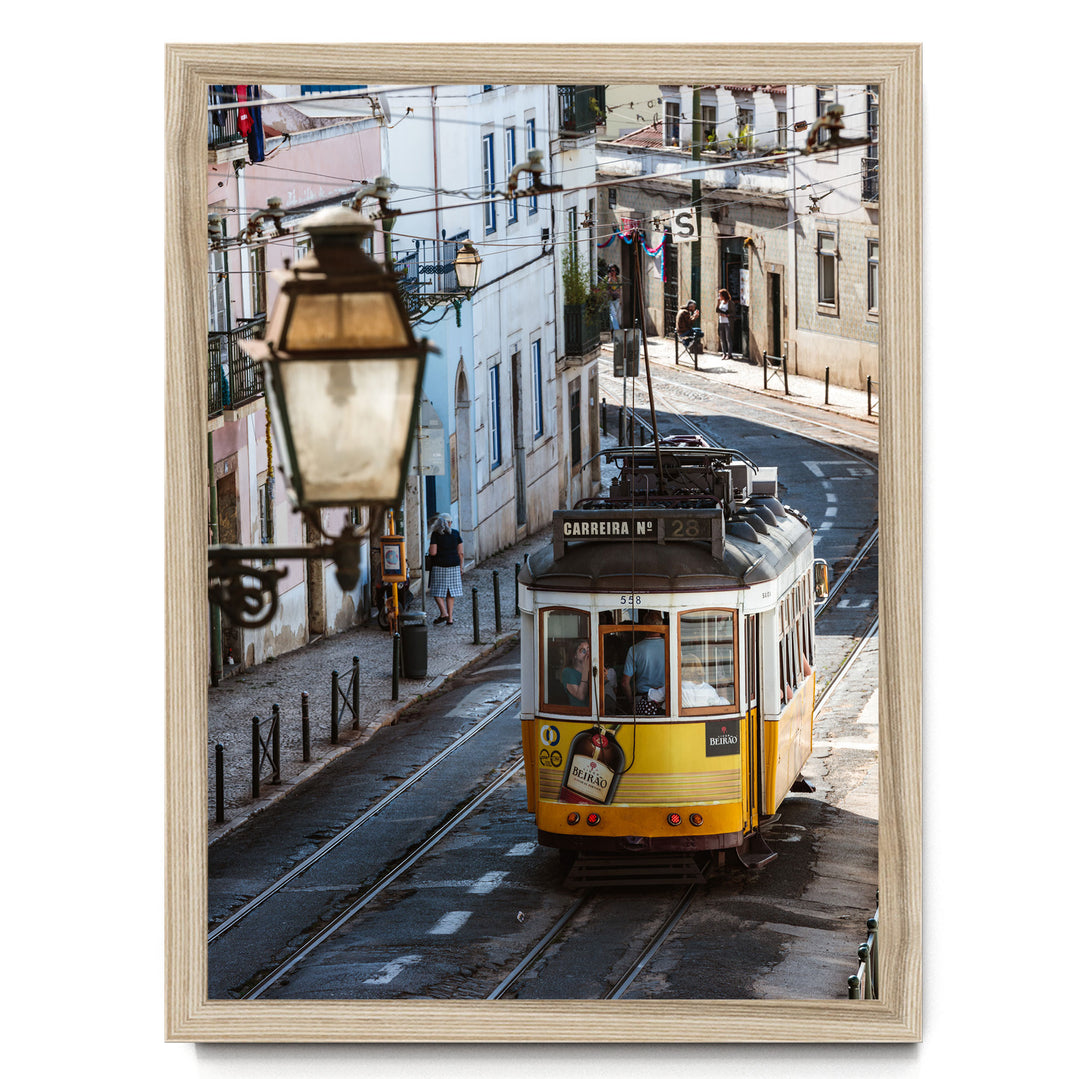 A yellow tram is traveling down a street lined with buildings and a lamppost.