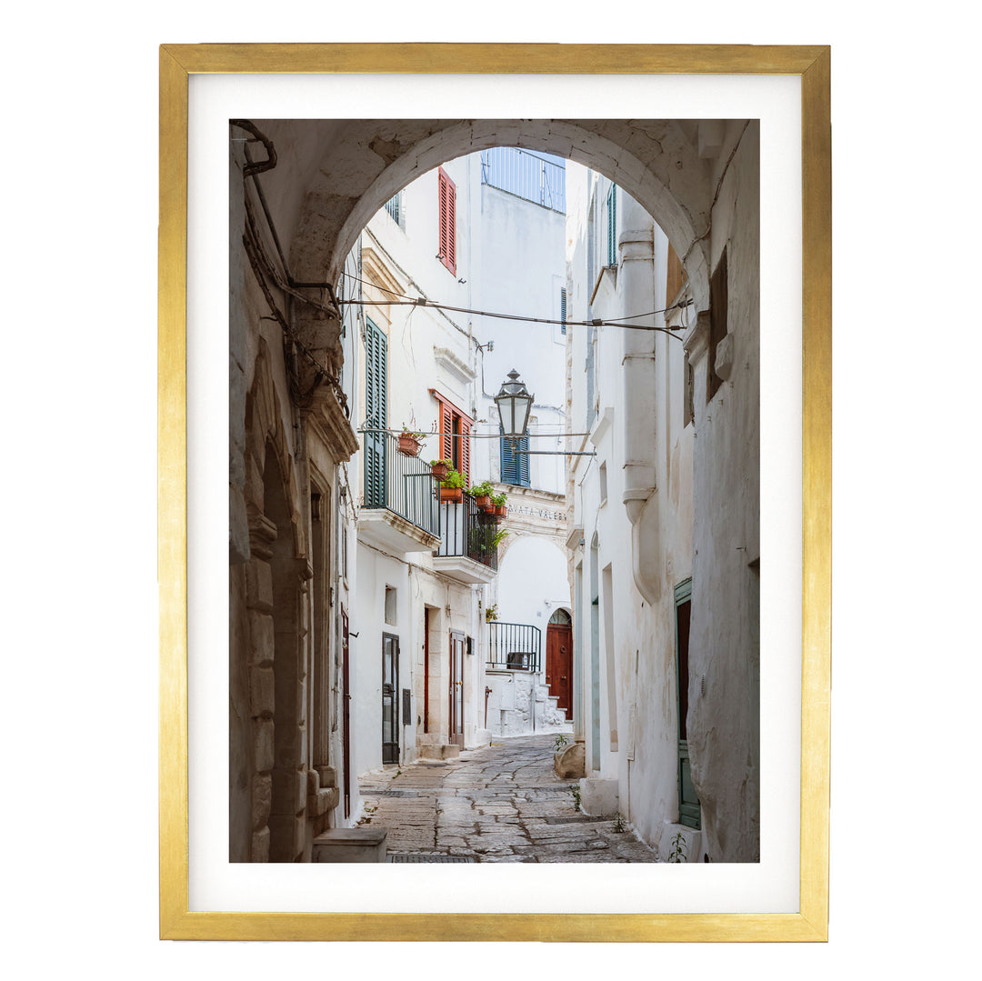 a narrow, cobblestone street lined with white buildings featuring arched doorways and balconies.