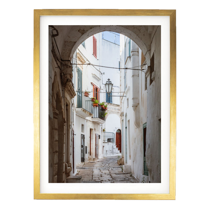 a narrow, cobblestone street lined with white buildings featuring arched doorways and balconies.