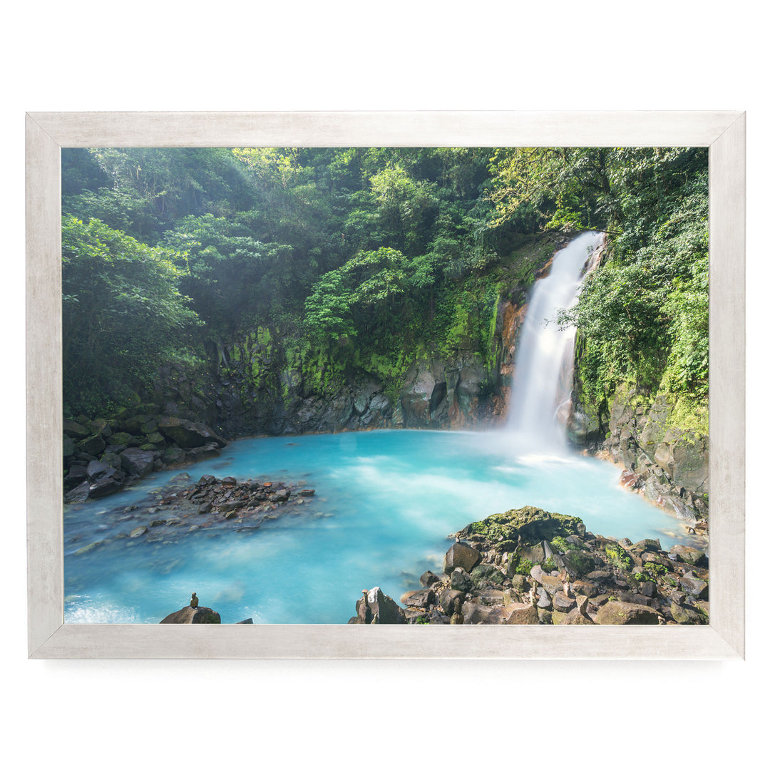 A serene waterfall cascades into a turquoise pool surrounded by lush, verdant foliage in a tranquil forest setting.