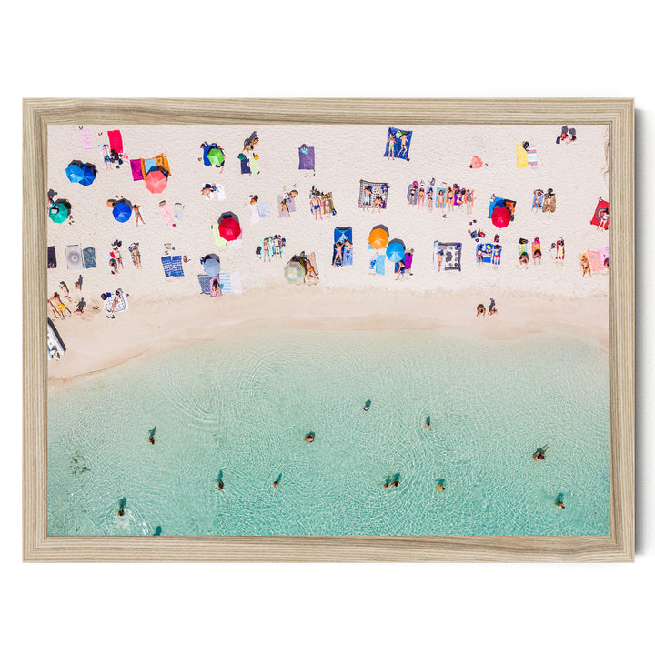 a crowded beach with numerous people enjoying the sunny day, some swimming in the clear blue water, and others relaxing on colorful beach towels and umbrellas.