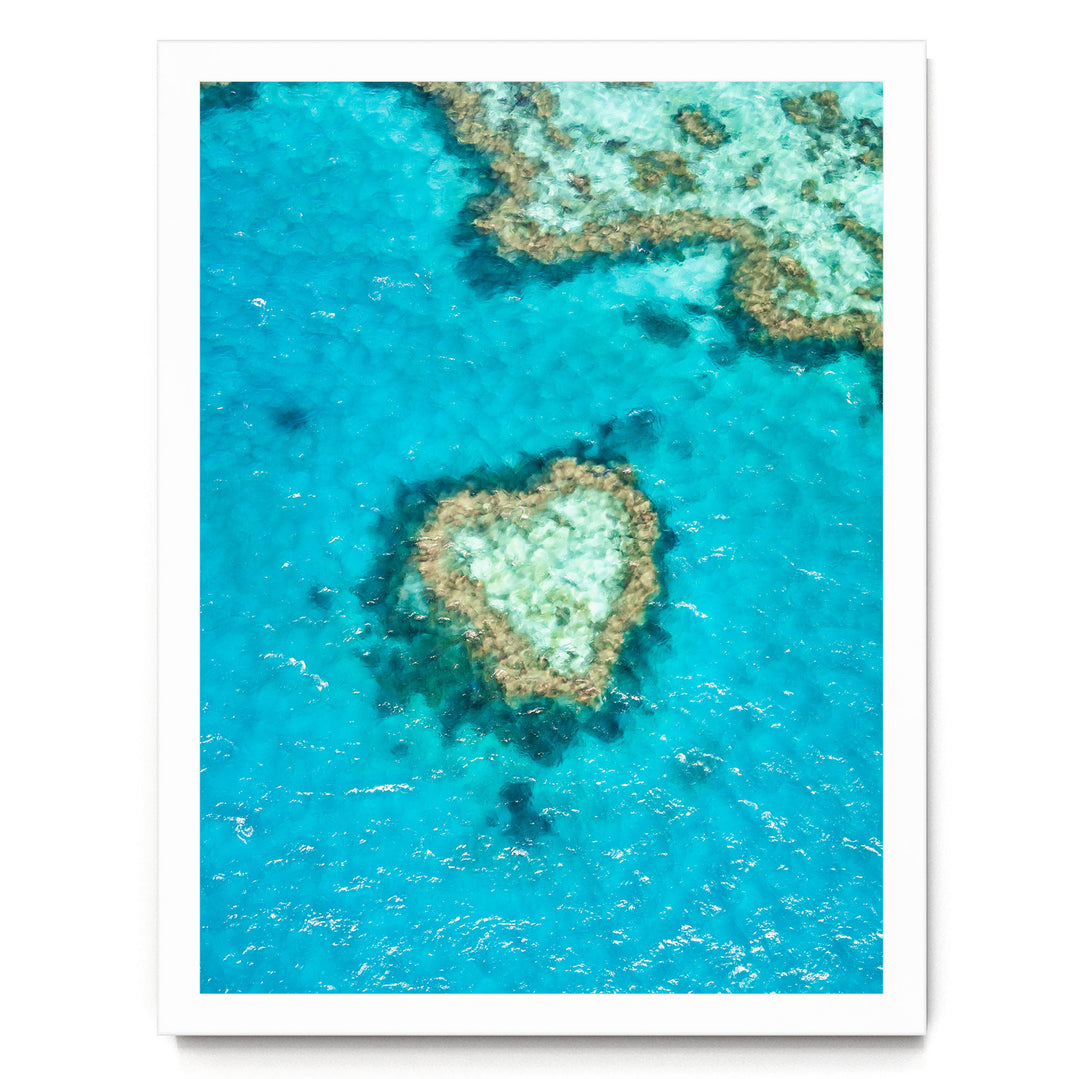 An aerial view of a vibrant coral reef, with a heart-shaped coral formation in the center surrounded by the blue-green waters.