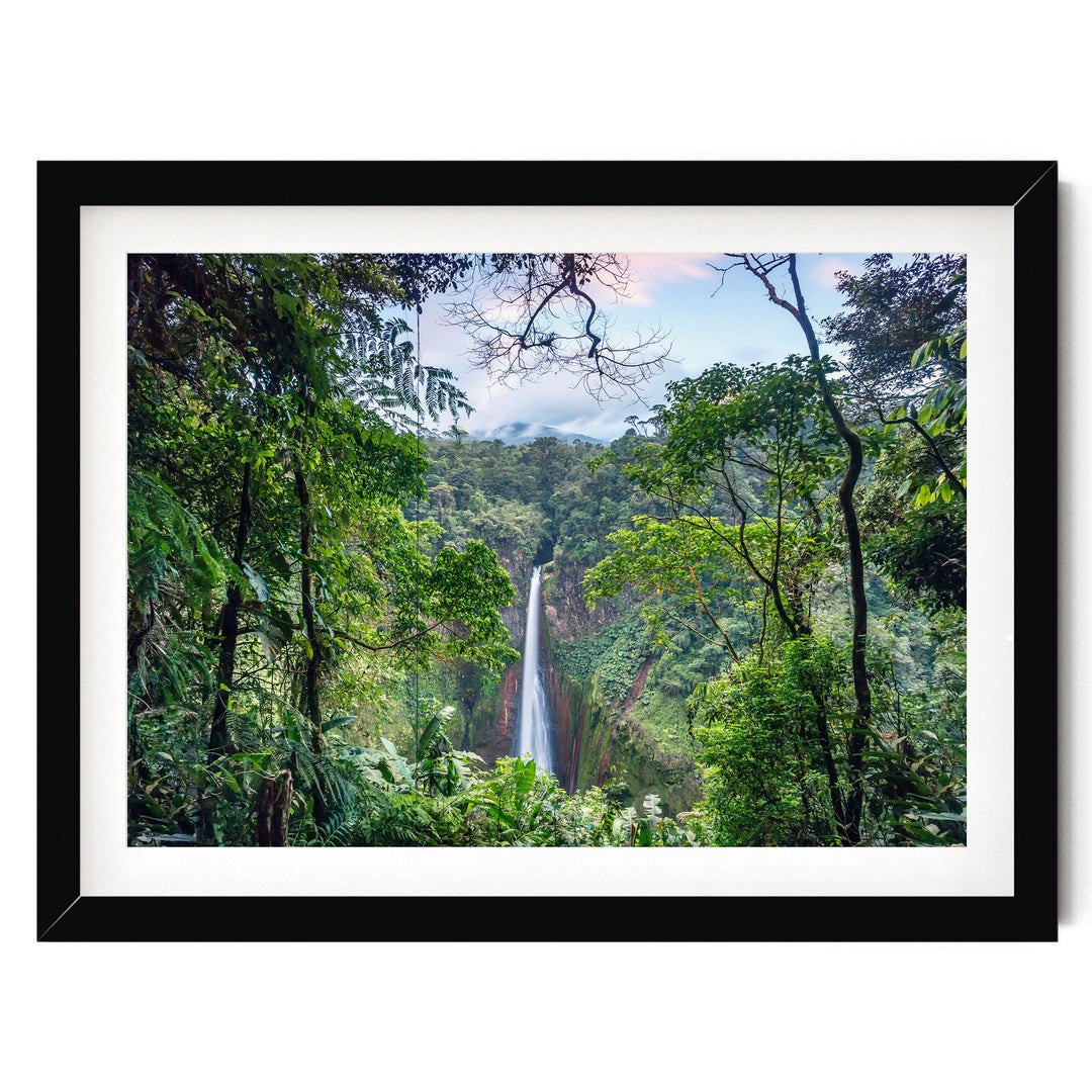 A lush, verdant forest with a towering waterfall cascading down the rocky cliff face, framed in a black border.