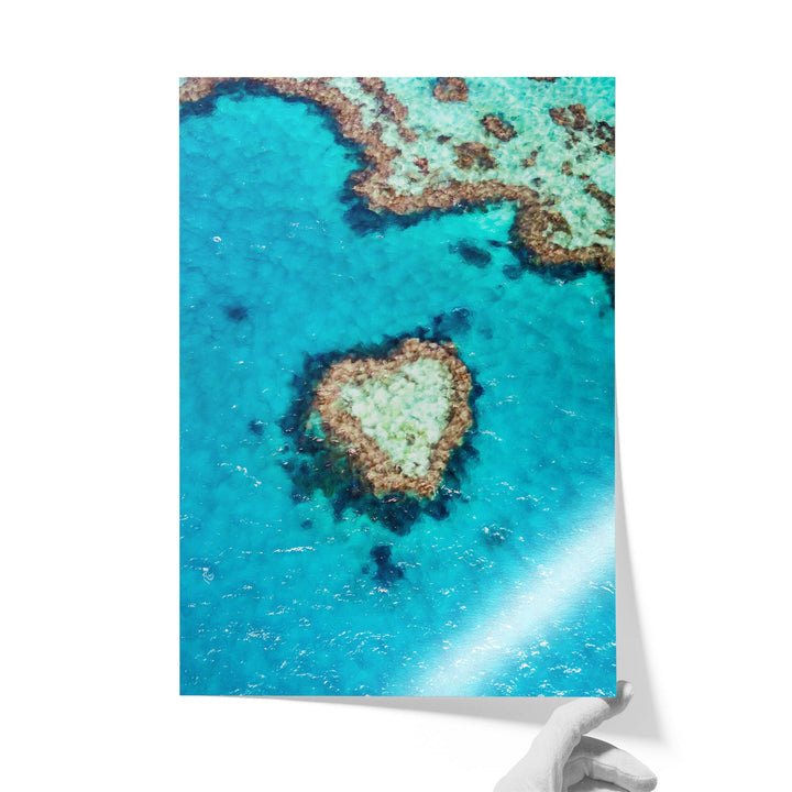 The image is a photograph of a coral reef in the ocean, featuring a heart-shaped coral formation surrounded by the vibrant blue waters.