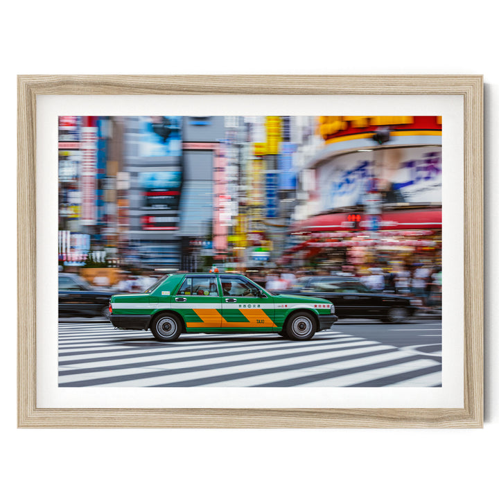 A green and yellow taxi cab is driving on a busy city street, surrounded by tall buildings and blurred pedestrians.