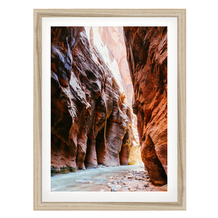 A framed photograph depicting a narrow, winding river flowing through a canyon with towering red rock walls on either side.