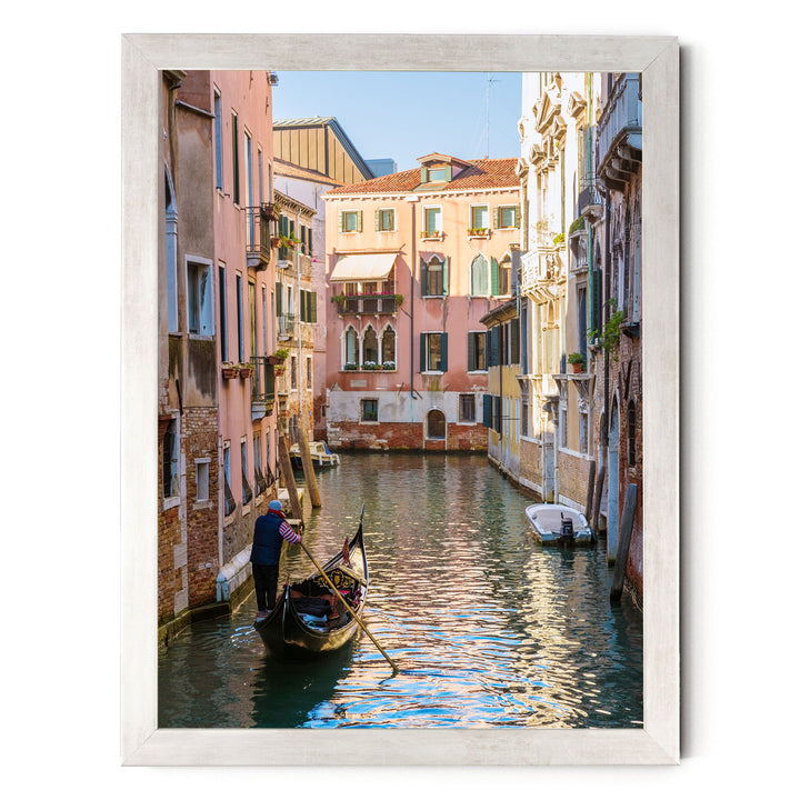 A gondolier in a traditional Venetian gondola navigates a picturesque canal in Venice, surrounded by colorful buildings and reflecting the warm sunlight.