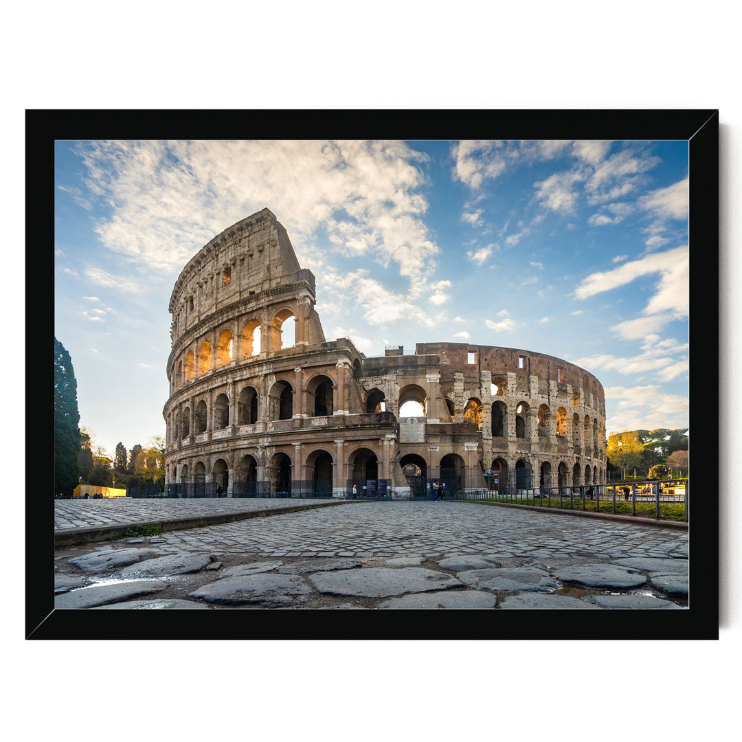 the Colosseum, an ancient amphitheater in Rome, Italy, with its distinctive oval shape and arches. The Colosseum is set against a backdrop of a blue sky with clouds, creating a picturesque scene.