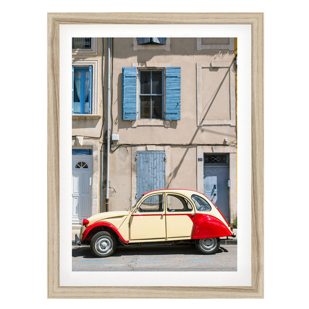A vintage red and cream-colored car is parked on a street in front of a building with blue shutters and a white door.