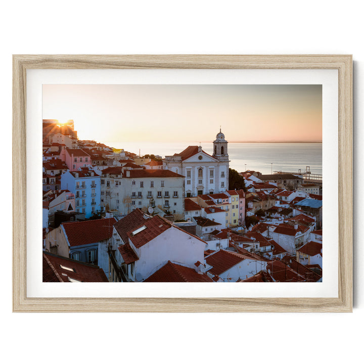 a picturesque town with a church and colorful buildings set against a backdrop of a sunset over the ocean.