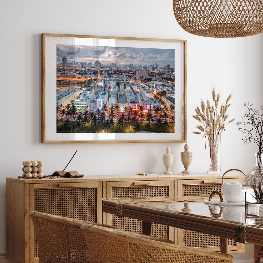 a large framed picture of a cityscape hanging on a wall above a wooden cabinet with drawers. The cabinet has a glass top and is situated in a dining area with a table and chairs. The overall setting appears to be a modern and stylish interior design.