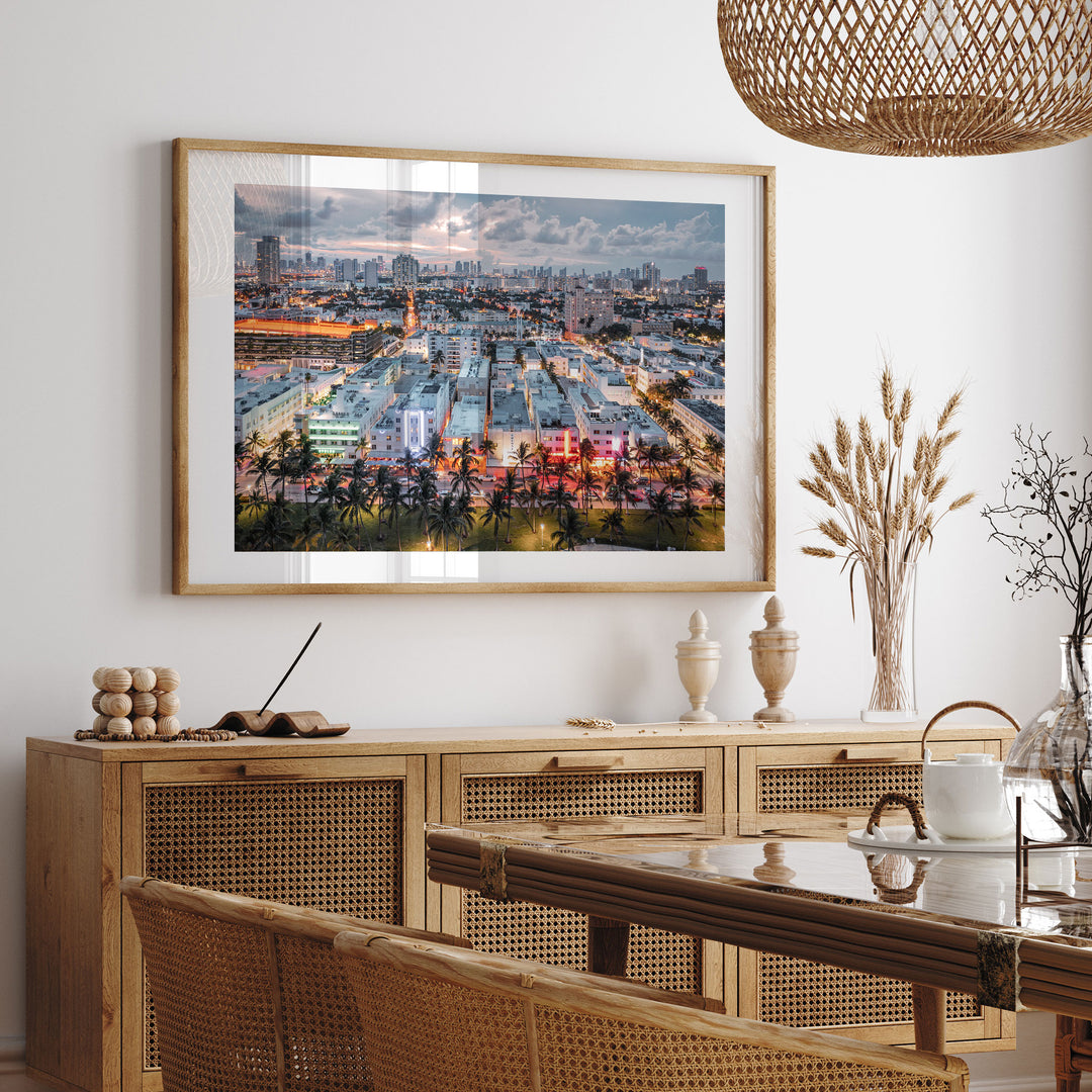 a large framed picture of a cityscape hanging on a wall above a wooden cabinet with drawers. The cabinet has a glass top and is situated in a dining area with a table and chairs. The overall setting appears to be a modern and stylish interior design.