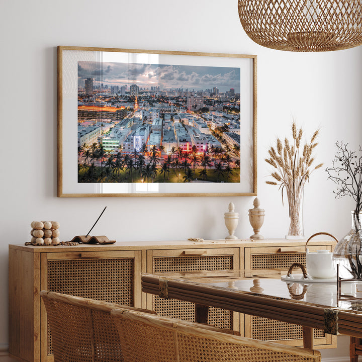 a large framed picture of a cityscape hanging on a wall above a wooden cabinet with drawers. The cabinet has a glass top and is situated in a dining area with a table and chairs. The overall setting appears to be a modern and stylish interior design.