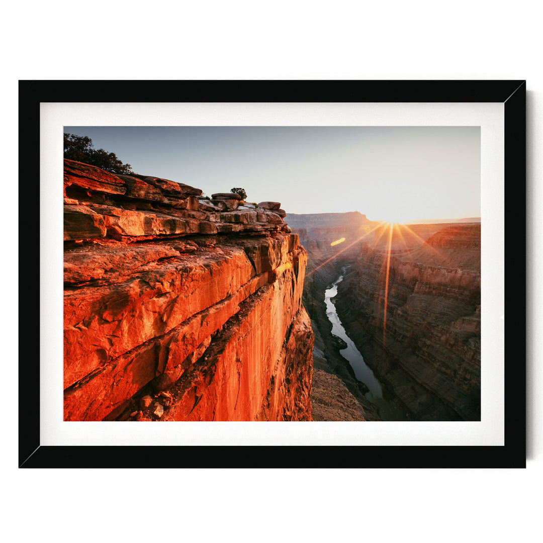 A framed photograph depicting a dramatic canyon landscape with a river flowing through it, set against a backdrop of a bright, sun-drenched sky.