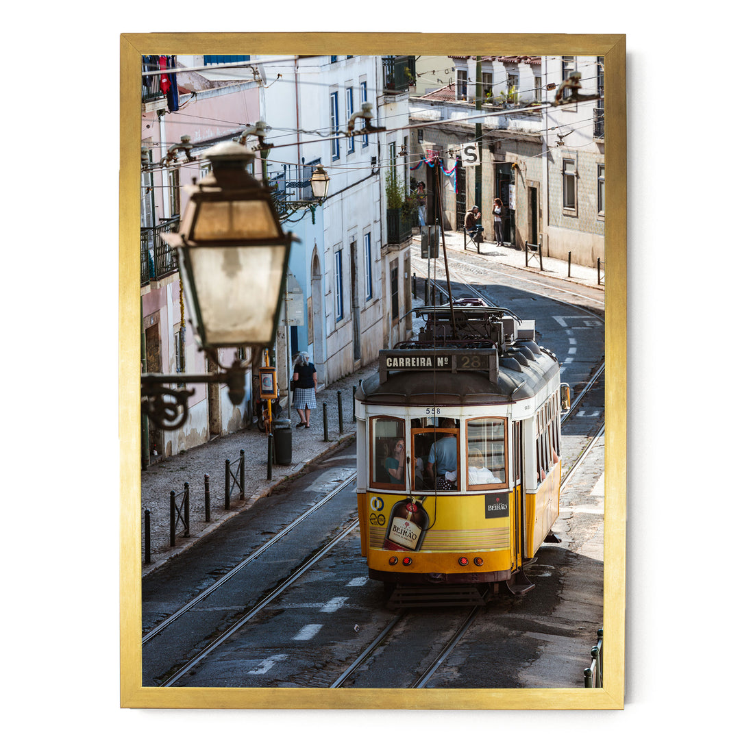 A yellow tram is traveling down a street lined with buildings and a lamppost.