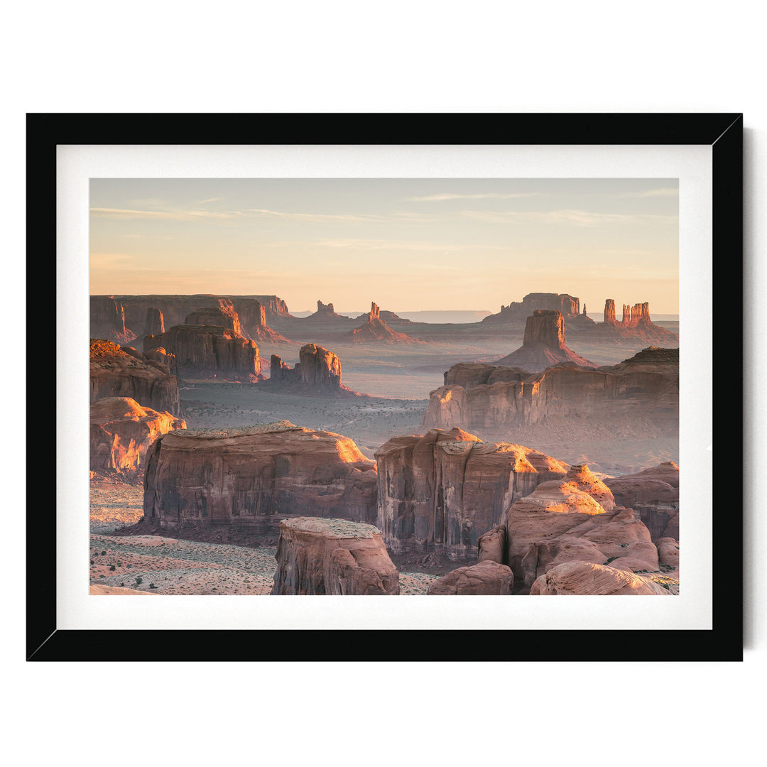 a breathtaking view of the Grand Canyon, with its towering red rock formations bathed in the warm glow of the setting sun. The sky above is a beautiful canvas of orange and pink hues, creating a stunning backdrop for the natural landscape. The photograph is framed and appears to be a high-quality image of the Grand Canyon, showcasing its grandeur and beauty.