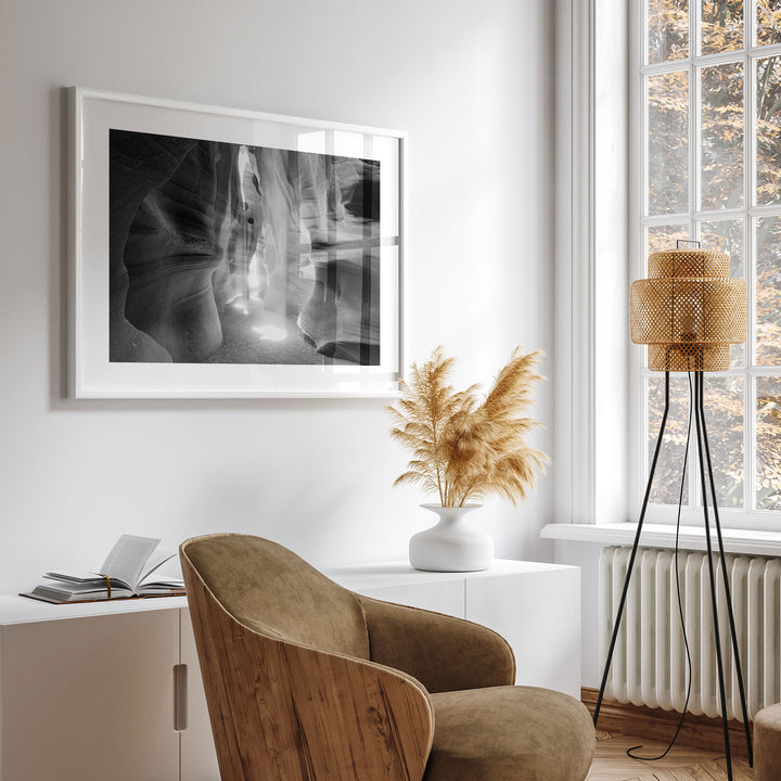 a modern living room with a large framed black and white photograph of a canyon or rock formation on the wall, a wooden chair, a white side table with a vase of dried flowers, and a floor lamp with a woven base.