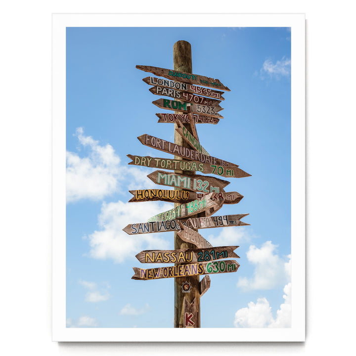 A wooden signpost with various destinations written on it, pointing in different directions against a blue sky with clouds.
