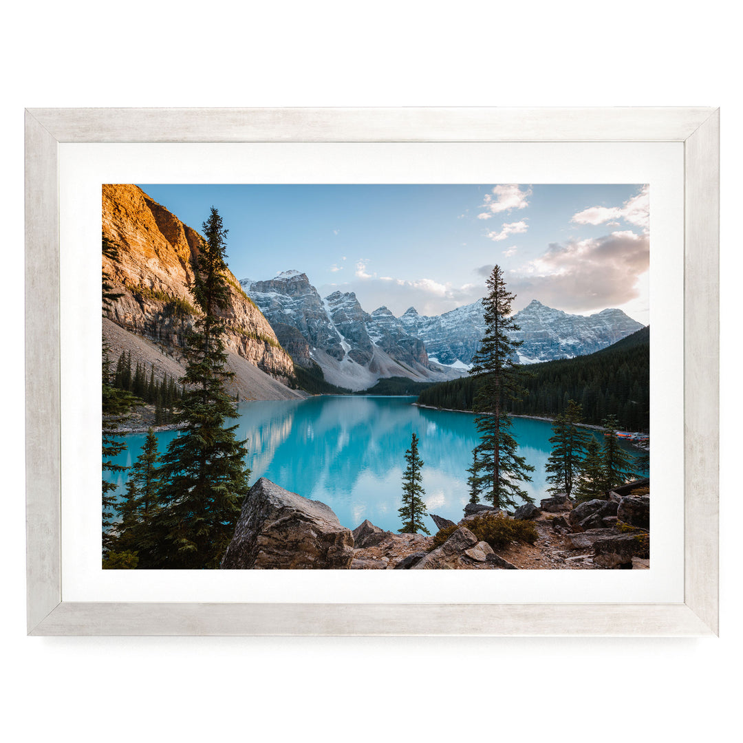 A framed photograph depicting a serene mountain landscape with a deep blue lake surrounded by snow-capped peaks and pine trees.