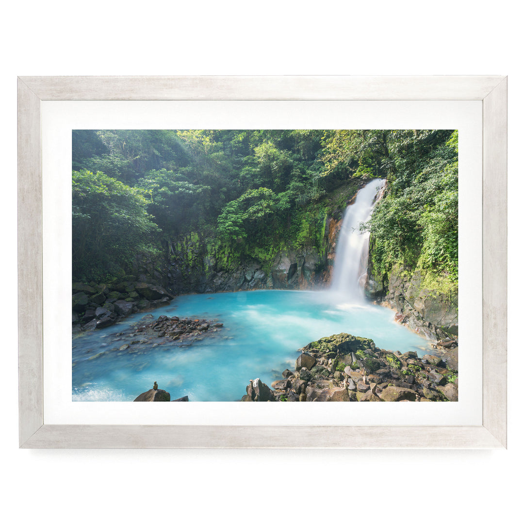 A serene waterfall cascades into a turquoise pool surrounded by lush, verdant foliage in a tranquil forest setting.