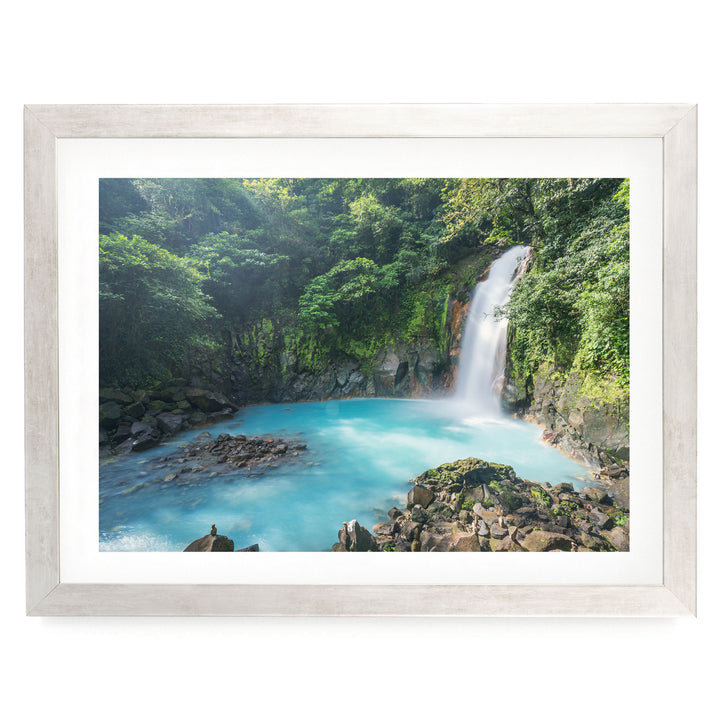 A serene waterfall cascades into a turquoise pool surrounded by lush, verdant foliage in a tranquil forest setting.