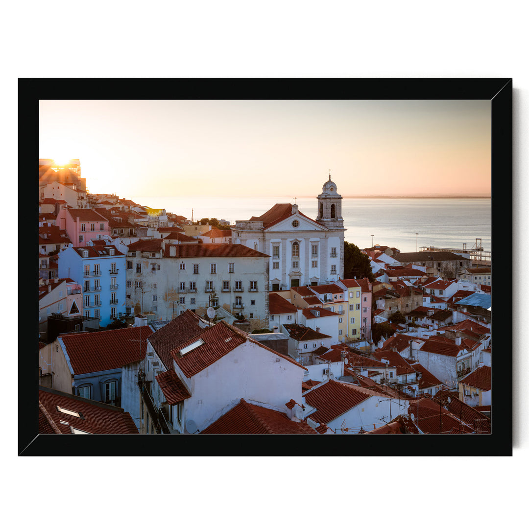 a picturesque town with a mix of white and red-tiled roofs, surrounded by the ocean. The sun is setting, casting a warm glow over the scene and highlighting the architectural details of the buildings.