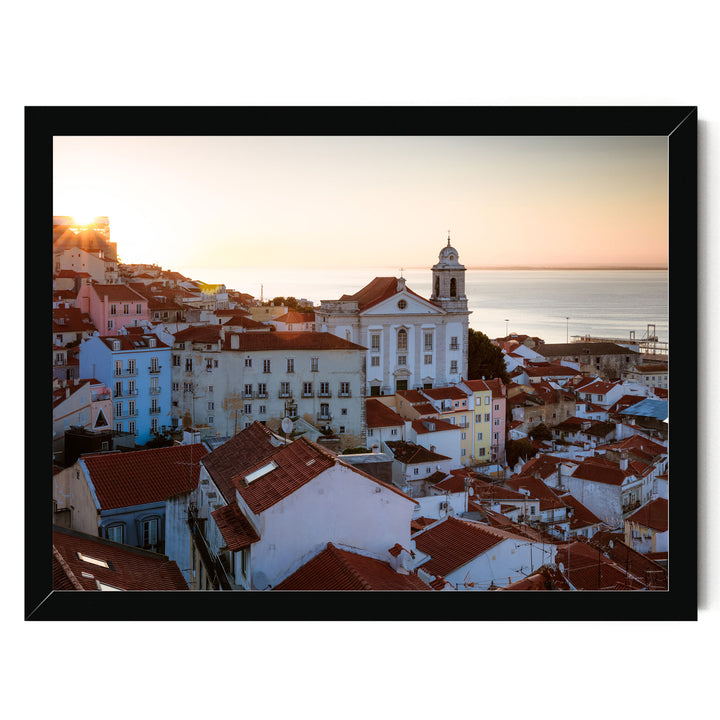 a picturesque town with a mix of white and red-tiled roofs, surrounded by the ocean. The sun is setting, casting a warm glow over the scene and highlighting the architectural details of the buildings.